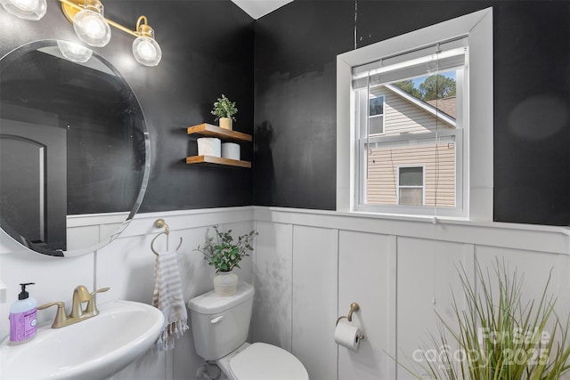 bathroom featuring a sink, a decorative wall, a wainscoted wall, and toilet