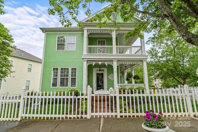 neoclassical home with a porch, a balcony, and a fenced front yard