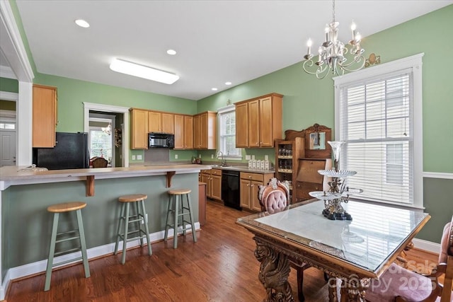 kitchen featuring a chandelier, a breakfast bar area, light countertops, black appliances, and a peninsula
