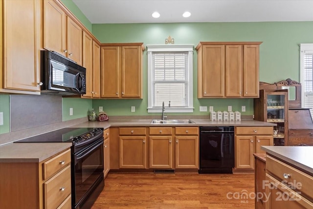 kitchen with black appliances, a sink, light countertops, and light wood-type flooring