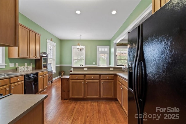 kitchen featuring brown cabinets, a chandelier, black appliances, a peninsula, and wood finished floors