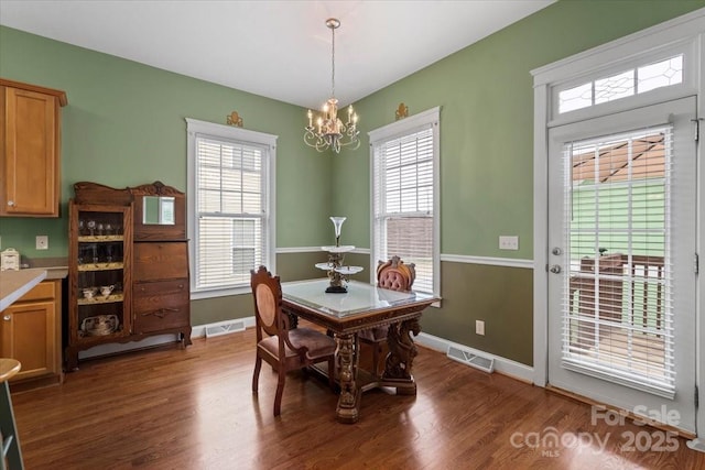 dining area with a wealth of natural light, visible vents, a notable chandelier, and dark wood-type flooring