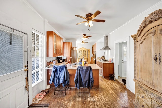 kitchen featuring a peninsula, wood finished floors, ceiling fan, light countertops, and wall chimney exhaust hood