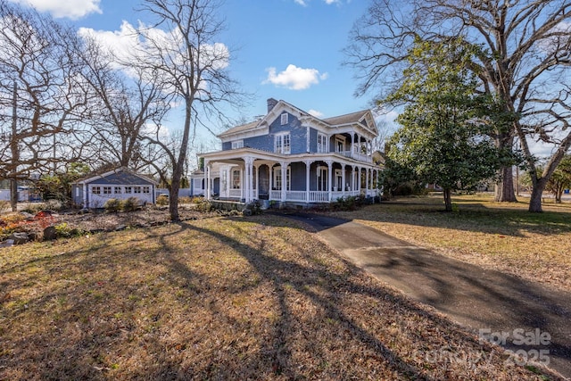 view of front of property with covered porch, a chimney, driveway, and a front yard