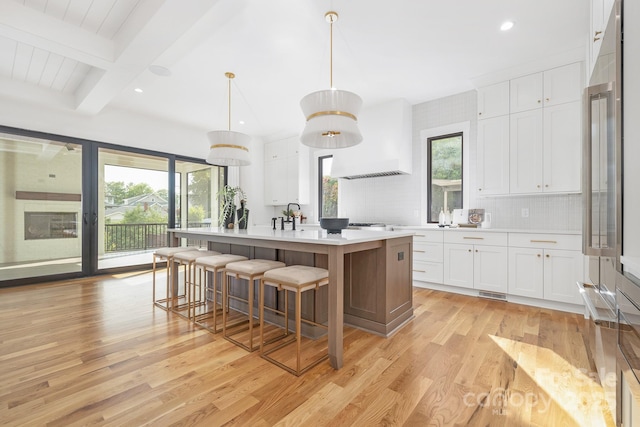 632 Dorothy Dr, Charlotte, NC 28203 - kitchen featuring custom exhaust hood, light wood-style floors, light countertops, an island with sink, and tasteful backsplash
