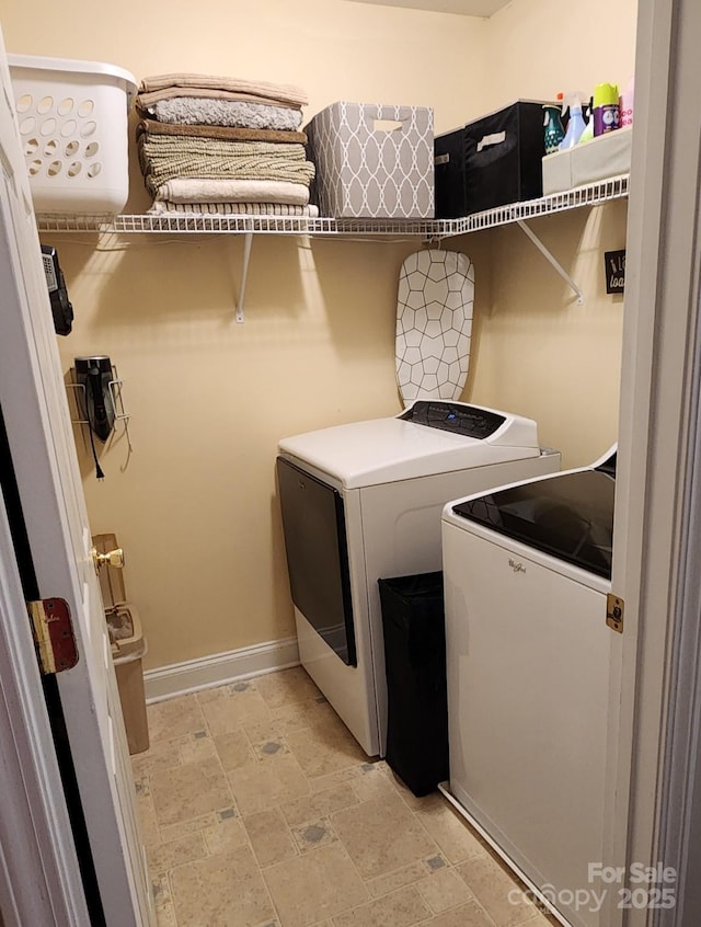 clothes washing area featuring washing machine and dryer, laundry area, baseboards, and stone finish floor
