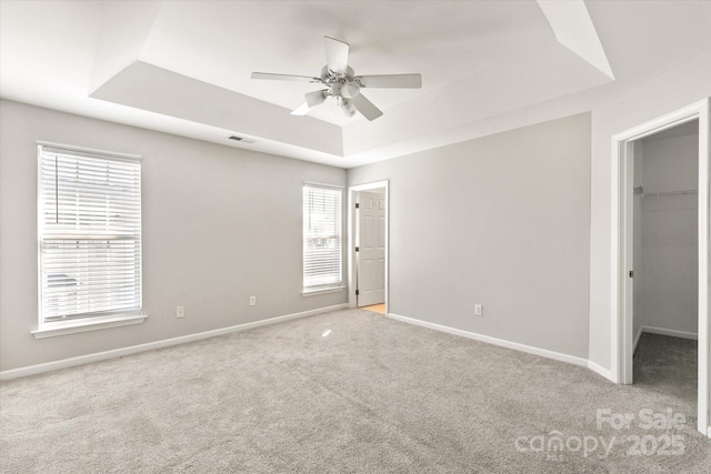 unfurnished bedroom with baseboards, carpet flooring, a raised ceiling, and a spacious closet