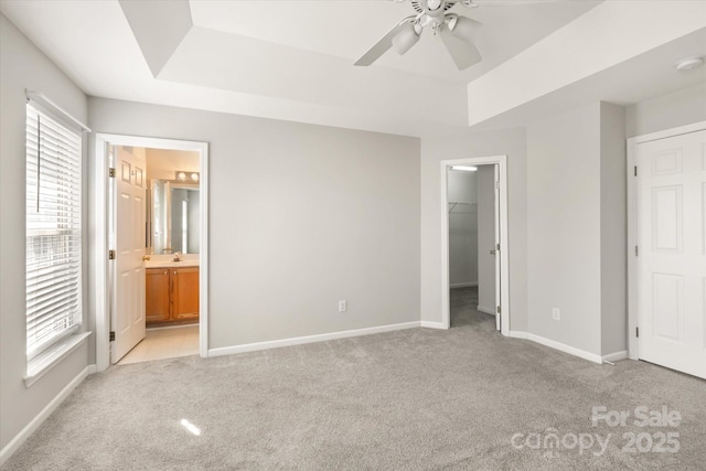 unfurnished bedroom with baseboards, light colored carpet, a walk in closet, and a raised ceiling