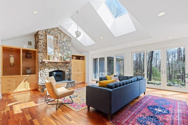 living area with a skylight, a stone fireplace, french doors, and light wood-style flooring