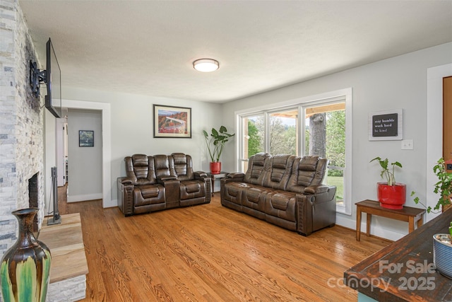 living area featuring light wood-type flooring, a stone fireplace, and baseboards
