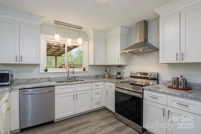 kitchen featuring wall chimney exhaust hood, a sink, appliances with stainless steel finishes, and white cabinetry