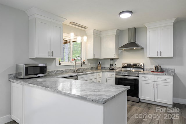 kitchen with a sink, light wood-style floors, a peninsula, wall chimney range hood, and appliances with stainless steel finishes