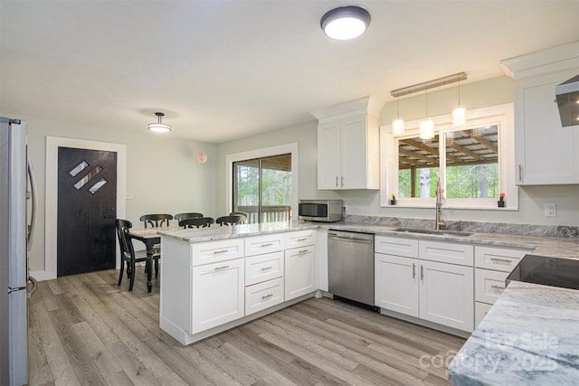 kitchen with pendant lighting, white cabinets, a sink, appliances with stainless steel finishes, and a peninsula