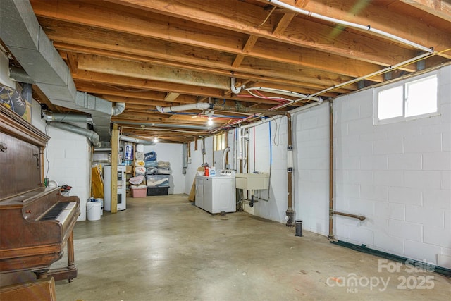 below grade area featuring concrete block wall, water heater, and washing machine and clothes dryer