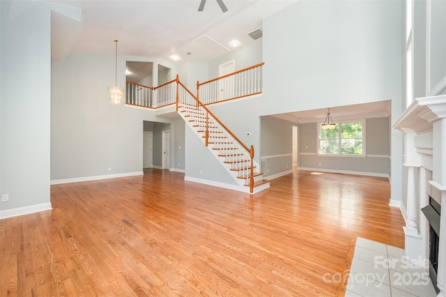 unfurnished living room featuring a high ceiling, a fireplace with flush hearth, light wood-type flooring, visible vents, and stairway