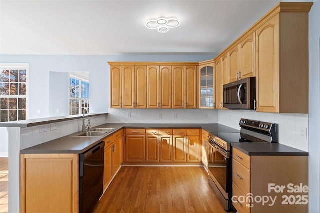 kitchen with a peninsula, dark countertops, a sink, light wood-style flooring, and stainless steel appliances