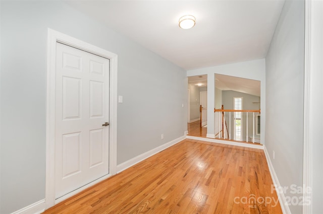 unfurnished room with baseboards, vaulted ceiling, and light wood-style flooring