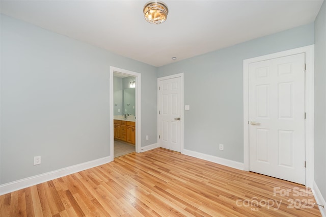 unfurnished bedroom with a sink, baseboards, ensuite bathroom, and light wood-style flooring