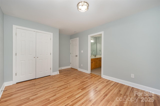 unfurnished bedroom featuring a closet, baseboards, ensuite bathroom, and light wood-type flooring