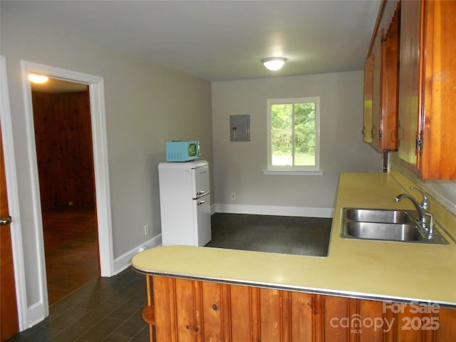 kitchen with brown cabinets, a peninsula, white microwave, and a sink
