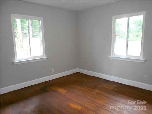 unfurnished room featuring plenty of natural light, dark wood finished floors, and baseboards