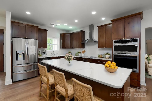 kitchen with dark brown cabinets, light wood finished floors, wall chimney exhaust hood, recessed lighting, and black appliances