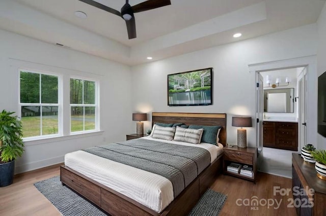 bedroom featuring wood finished floors, a raised ceiling, baseboards, connected bathroom, and recessed lighting