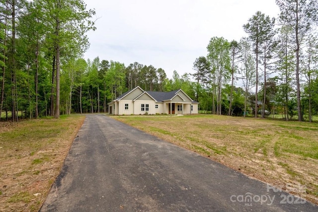 view of front of home with a view of trees, a front lawn, and aphalt driveway