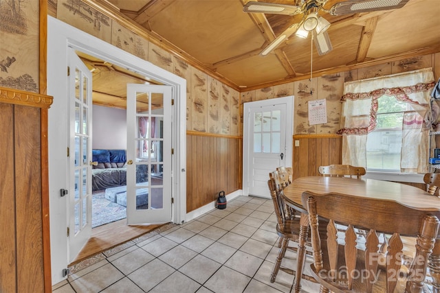 dining room featuring wooden walls, light tile patterned floors, ceiling fan, and baseboards