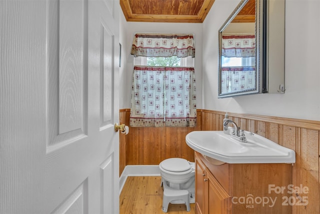 bathroom featuring vanity, wood walls, wood finished floors, toilet, and a wainscoted wall