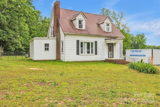 new england style home with fence, a chimney, metal roof, and a front lawn