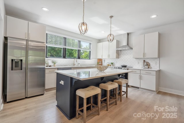kitchen with appliances with stainless steel finishes, wall chimney range hood, decorative backsplash, a breakfast bar area, and light countertops