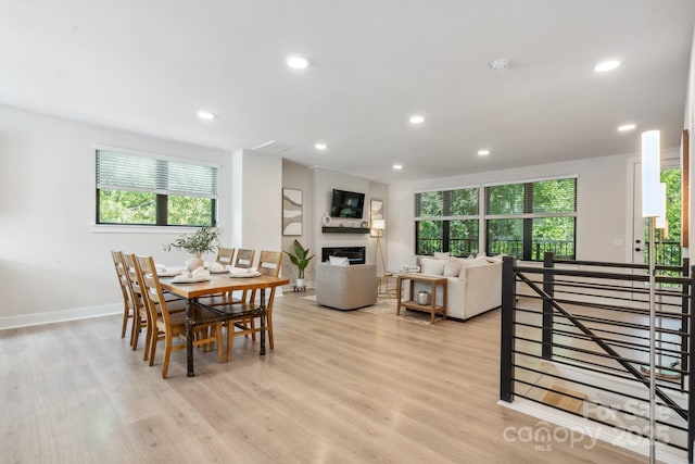 dining area featuring light wood finished floors, recessed lighting, a glass covered fireplace, and baseboards