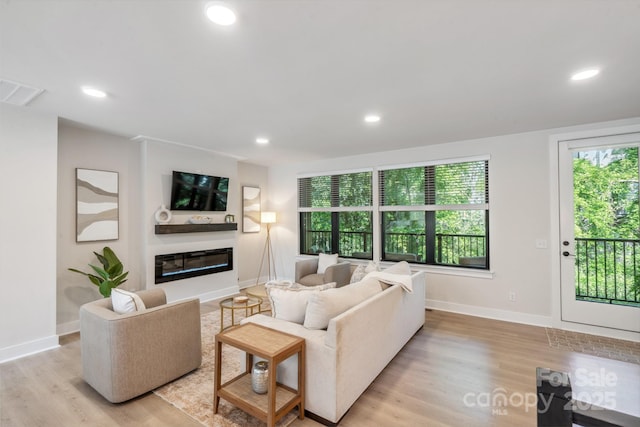 living room with light wood-type flooring, a glass covered fireplace, recessed lighting, and baseboards