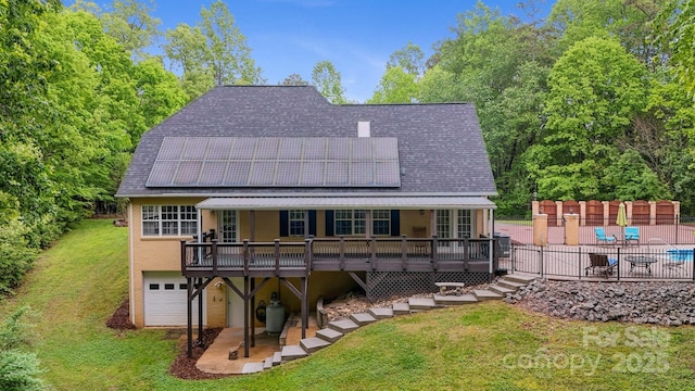 back of house featuring a wooden deck, a patio area, roof mounted solar panels, a yard, and an attached garage