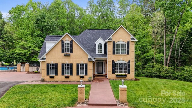 traditional-style home featuring an outdoor pool, a shingled roof, brick siding, and a front yard