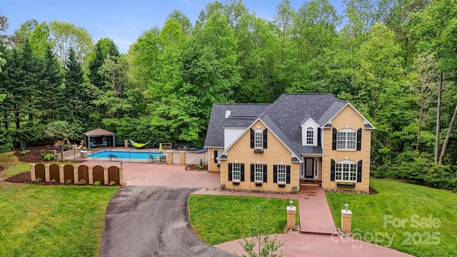 traditional home featuring roof with shingles, fence, a front lawn, and an outdoor pool