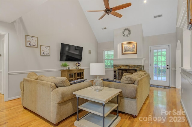 living room featuring a healthy amount of sunlight, ceiling fan, a stone fireplace, visible vents, and high vaulted ceiling