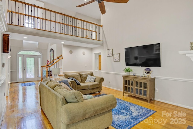 living room with light wood-style flooring, ceiling fan, a towering ceiling, and stairway