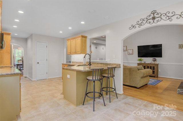 kitchen featuring light stone countertops, a sink, arched walkways, a kitchen breakfast bar, and recessed lighting