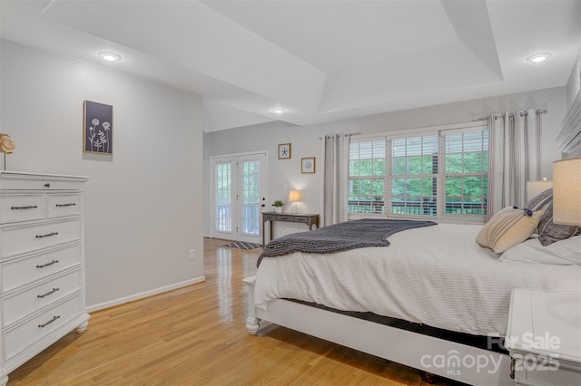 bedroom featuring a raised ceiling, multiple windows, baseboards, and light wood-style flooring