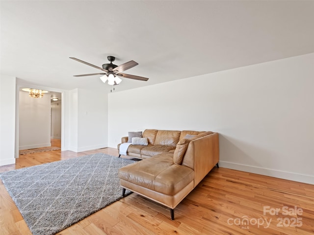 living area with light wood finished floors, ceiling fan with notable chandelier, and baseboards