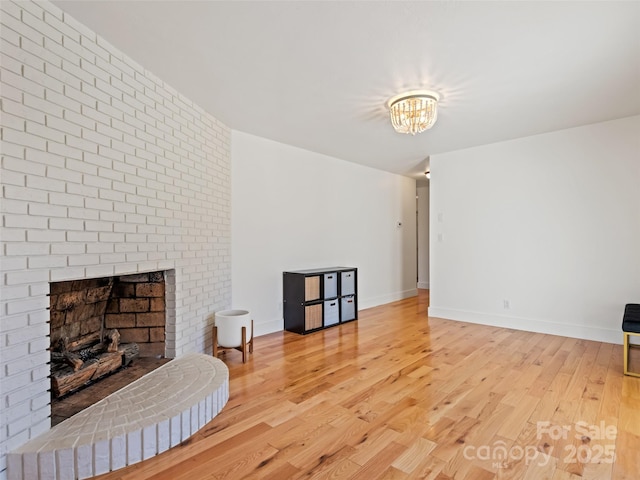 living area with an inviting chandelier, a fireplace, light wood-style flooring, and baseboards
