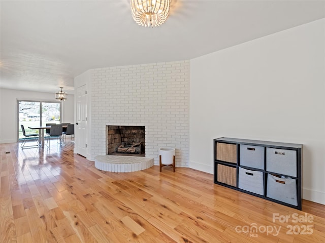 unfurnished living room featuring a brick fireplace, a notable chandelier, baseboards, and light wood-style floors