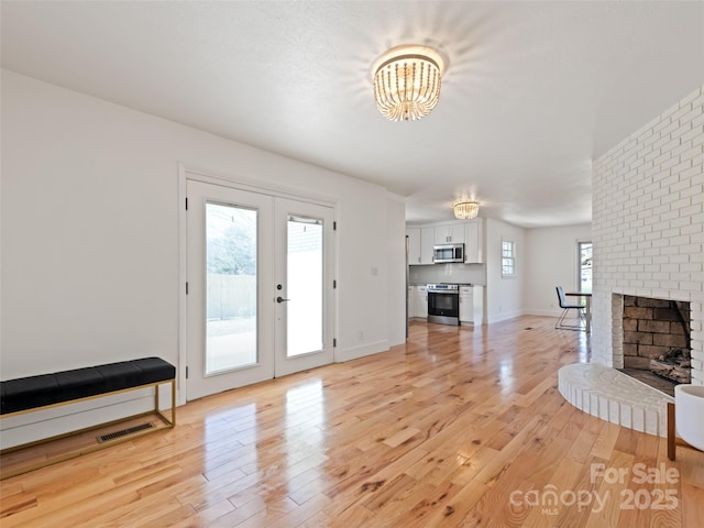 unfurnished living room with a fireplace, a notable chandelier, visible vents, light wood-style flooring, and french doors