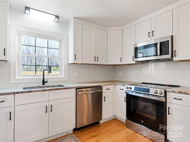 kitchen with light stone counters, white cabinetry, light wood-style flooring, a sink, and stainless steel appliances