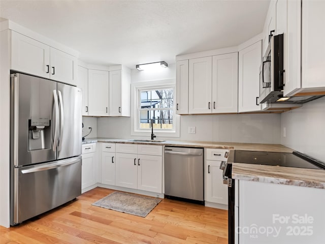 kitchen featuring light wood-style floors, stainless steel appliances, white cabinetry, and a sink