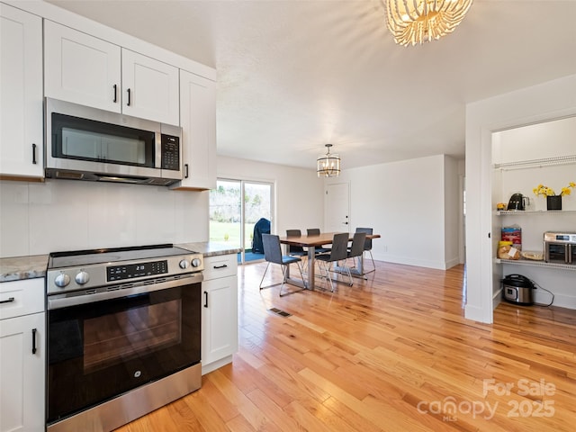 kitchen featuring white cabinets, light wood-type flooring, a notable chandelier, and appliances with stainless steel finishes