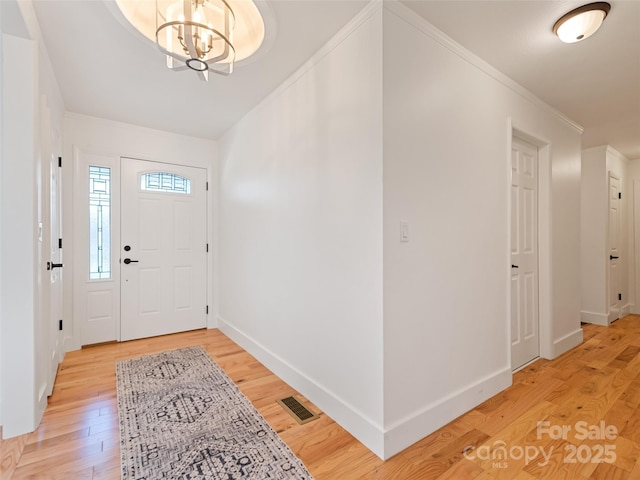 foyer with an inviting chandelier, light wood-type flooring, visible vents, baseboards, and ornamental molding