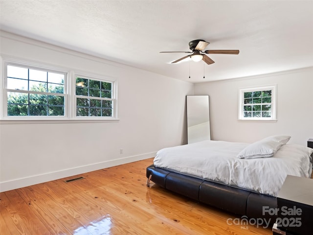 bedroom with light wood finished floors, visible vents, ceiling fan, and baseboards